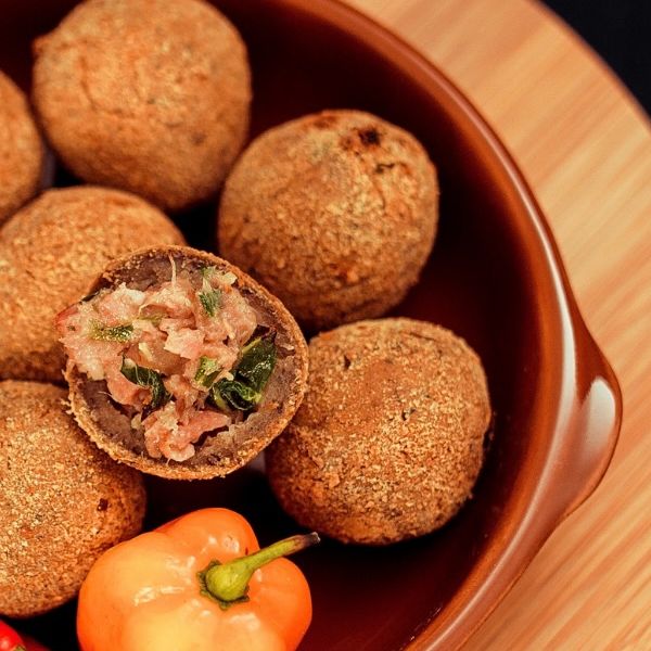 Bolinhos de feijoada numa cumbuca de barro, um deles aberto mostrando o recheio, com pimentas