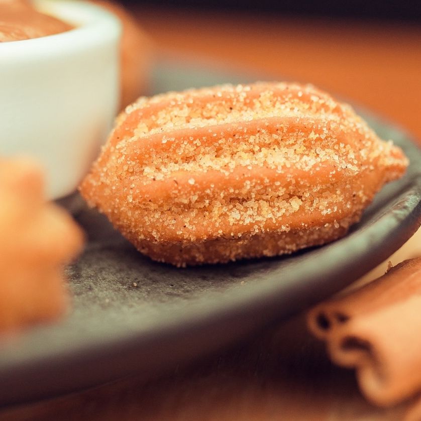 Churros de doce de leite passados no açúcar, num prato escuro, com canela em pau ao lado