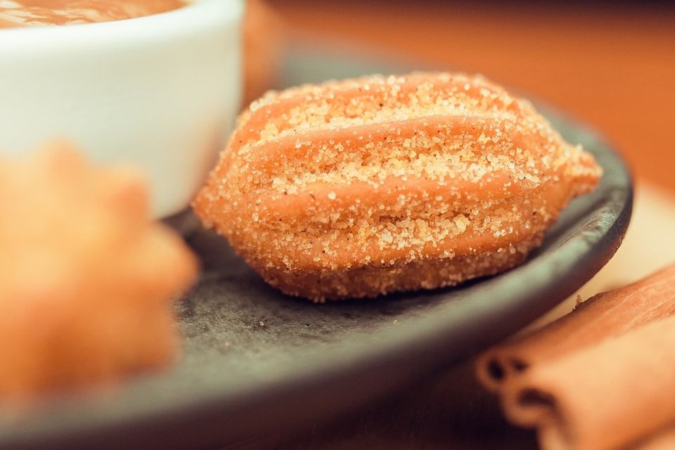 Churros de doce de leite passados no açúcar, num prato escuro, com canela em pau ao lado