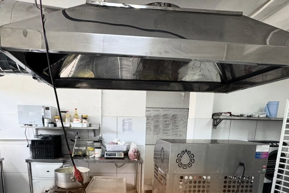 Cozinha de produção com coifa de inox, bancadas e um equipamento de inox