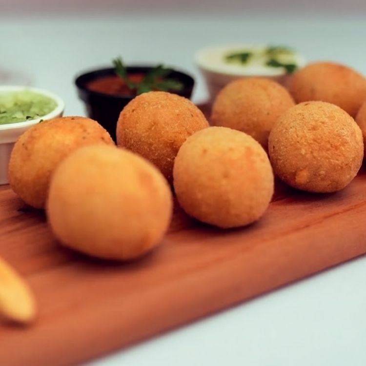Bolinhos fritos numa tábua de madeira, com três potinhos de molho ao fundo