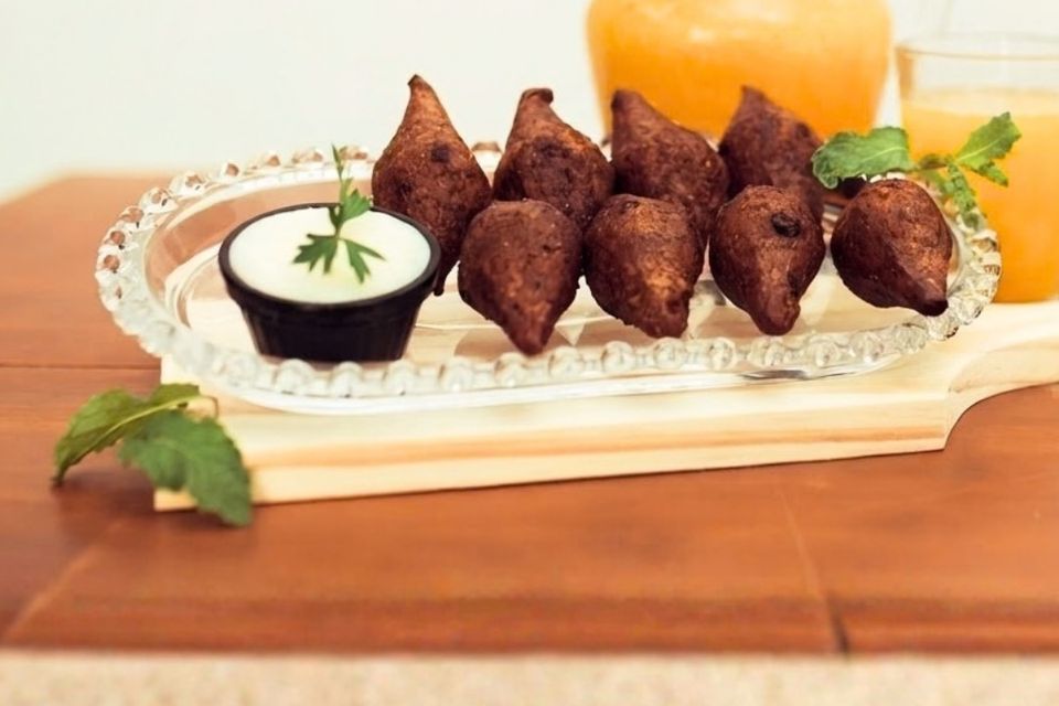 Quibes de carne numa travessa de vidro, com molho branco e folhas de hortelã, e suco ao fundo
