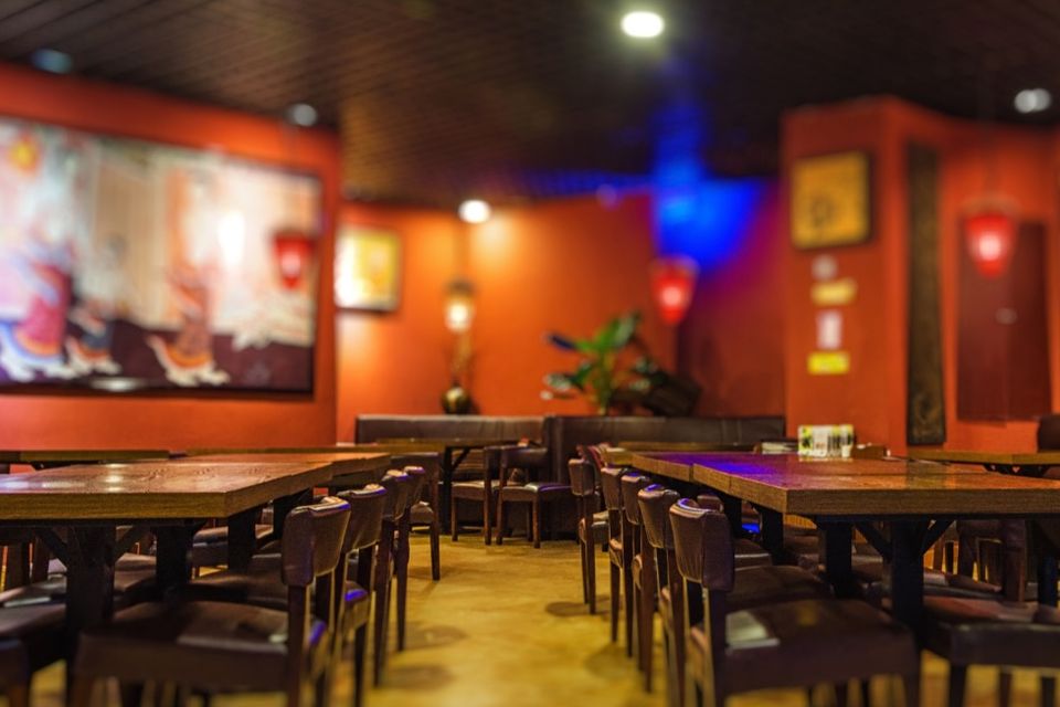 Salão de restaurante vazio, com mesas de madeira e paredes laranja